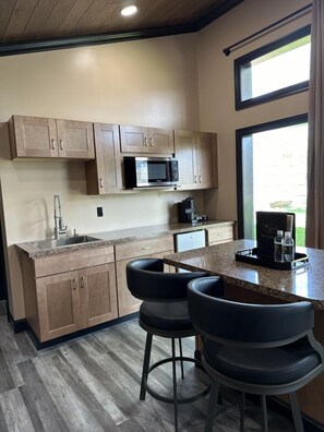 A modern kitchen with wooden cabinets, a built-in microwave, a sink, and a bar area with stools.