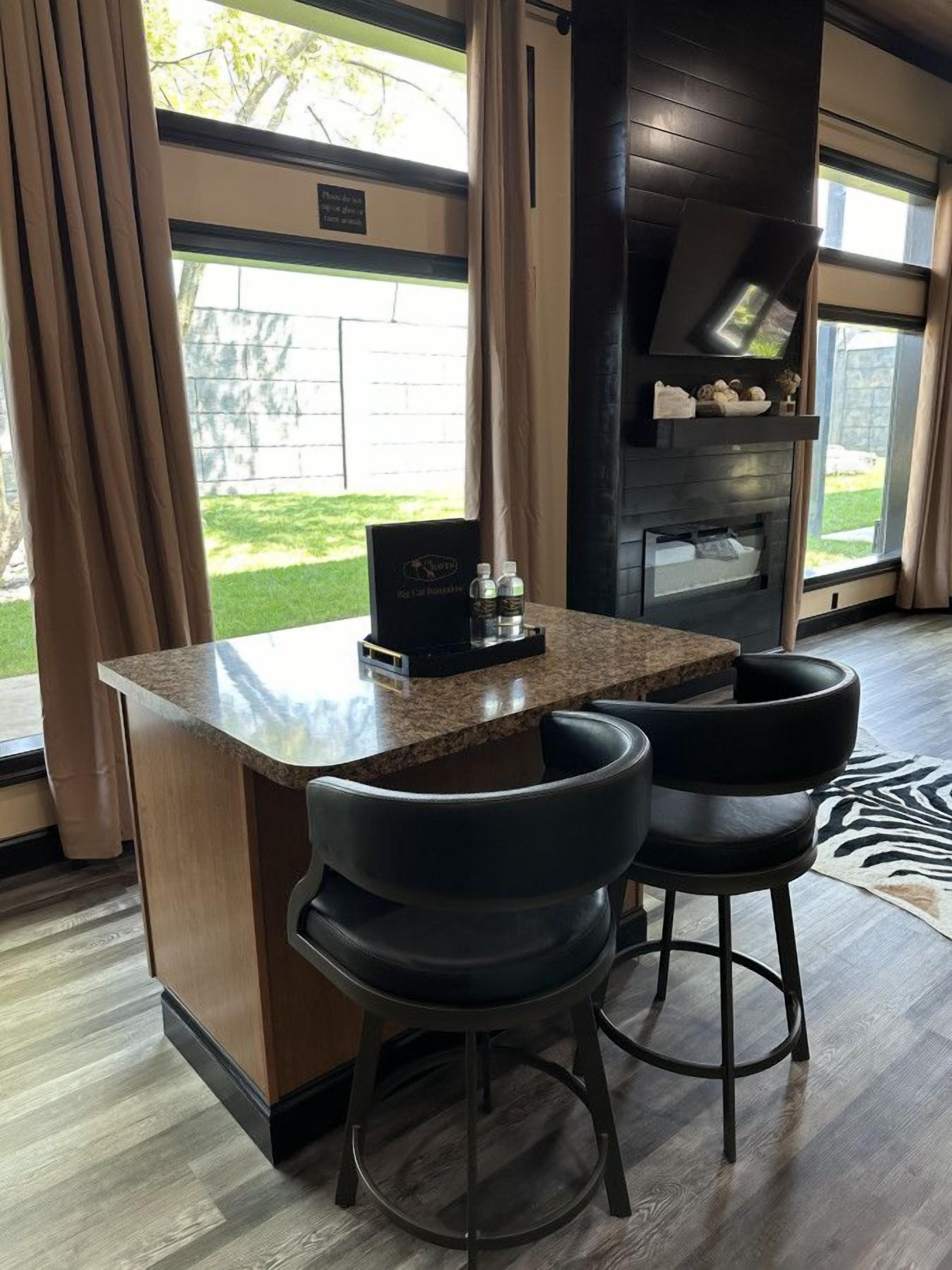 A bar area with a granite countertop, two black bar stools, and a television mounted on the wall.