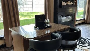 A bar area with a granite countertop, two black bar stools, and a television mounted on the wall.