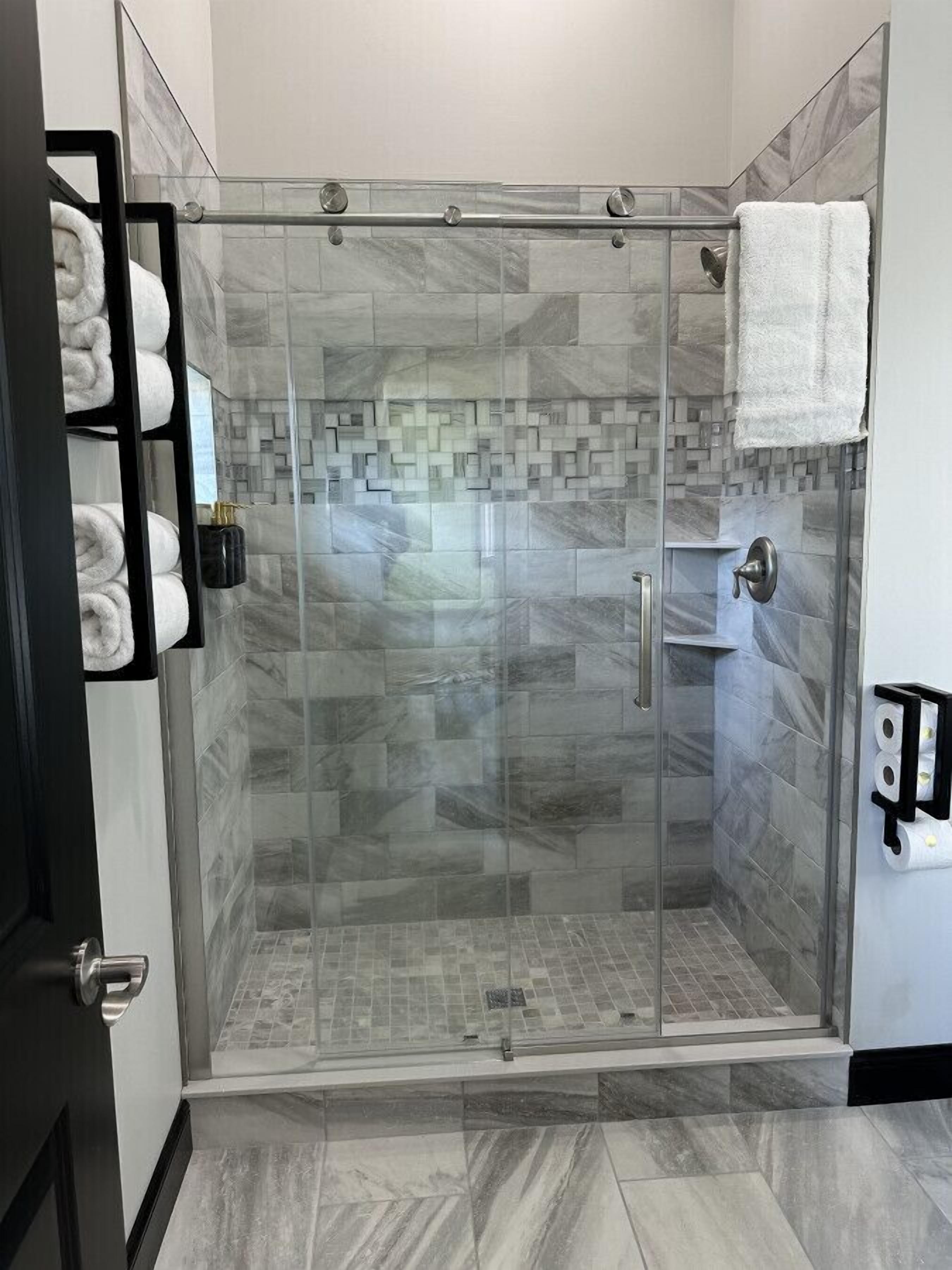 Una cabina doccia con pareti e pavimento piastrellati, un portasacchiuni con asciugamani e un porta carta igienica a parete.