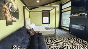 A cozy room with a dark sofa, a zebra-patterned rug, and a bed with a white headboard. - Big Cat Bungalows at The Haven - Tiger 4 (Chittenango)