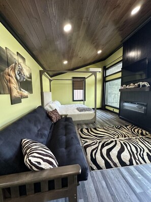 Een gezellige kamer met een donkere bank, een vloerkleed met zebraprint en een bed met een witte hoofdbord.