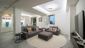 A modern living room with a sectional sofa, a round rug, and a flat-screen TV. - Villa Corito, luxury villa on the Amalfi coast (Campania)