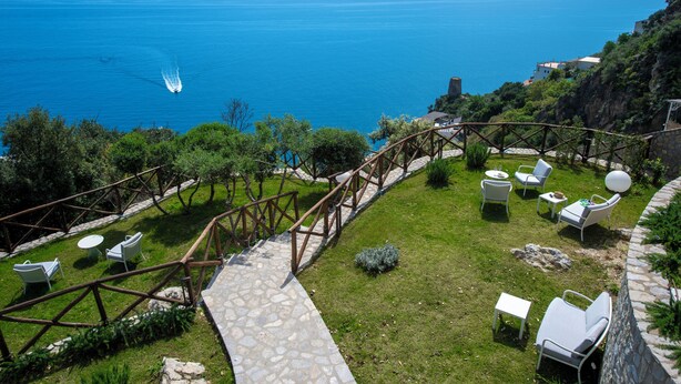 A terrace with stone flooring, white outdoor furniture, and a view of the sea. - Villa Corito, luxury villa on the Amalfi coast (Campania)