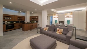 A modern kitchen with a central island, a dining area with a table and chairs, and a living room with a sofa and ottoman. - Villa Corito, luxury villa on the Amalfi coast (Campania)