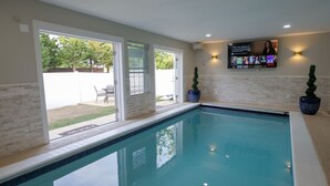 A swimming pool with a patio area, a television mounted on the wall, and a brick wall. - Private Indoor Swimming Pool (The Colony)