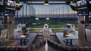 A modern viewing area with a central table, two sofas, and screens displaying golf courses. - Private Indoor Swimming Pool (The Colony)