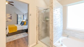 A modern bathroom with a glass shower enclosure, a bathtub, and a large window providing natural light. - Private Indoor Swimming Pool (The Colony)