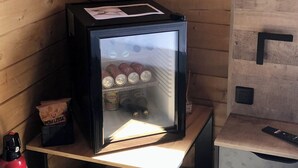 A small room with a refrigerator containing beverages, a fire extinguisher, and a wooden cabinet with a remote control. - Les Chalets de Tesa N°2 Luxe, Calme et Nature (Occhiatana)