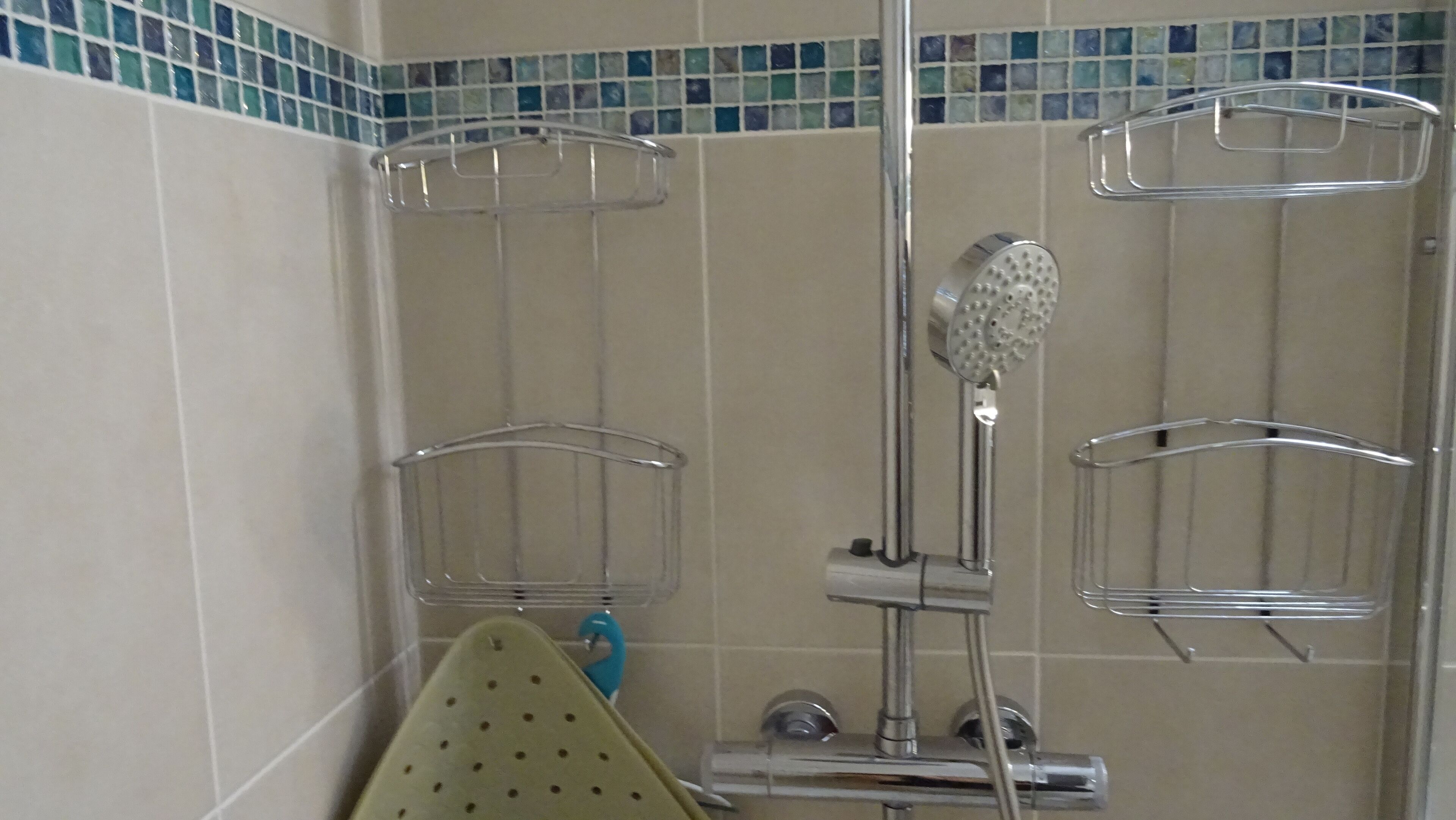 Zona de ducha con accesorios cromados, cabezal de ducha manual y dos cestas de ducha vacías.