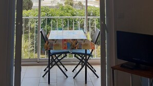 Quarto com ventoinha no teto, mesa com cadeiras, televisão e varanda com mesa e cadeiras.
