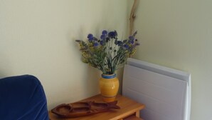 Um quarto pequeno com um sofá azul, uma mesa de madeira com um vaso de flores e um radiador na parede.