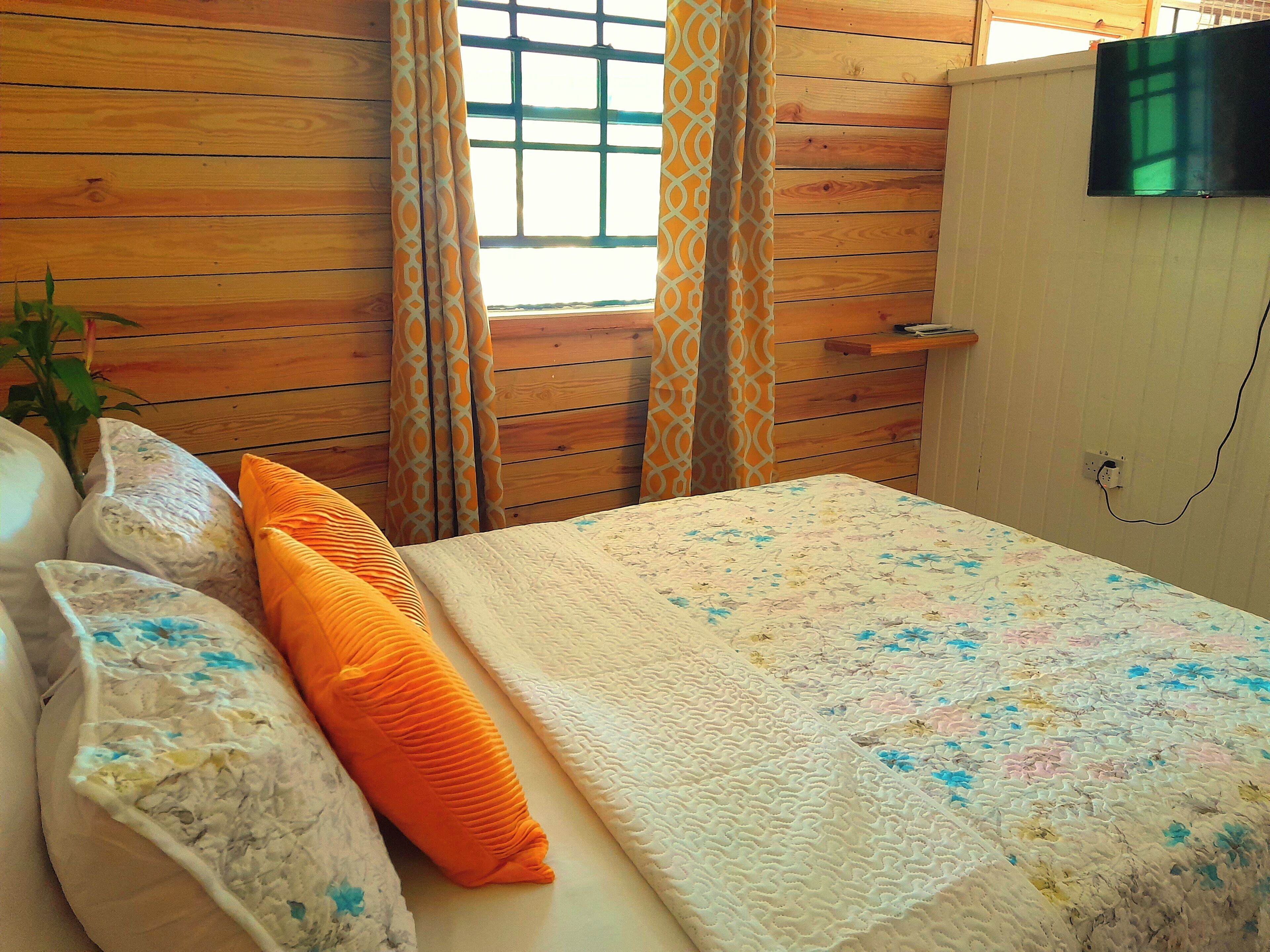 A bedroom with a wooden wall, a bed with a floral bedspread, two pillows, and a TV mounted on the wall.