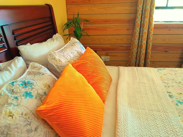 A bed with a floral-patterned pillow, a white pillow, and two orange pillows. - Pinard's Mountain Resort- Cottage 6 (Pointe Michel)