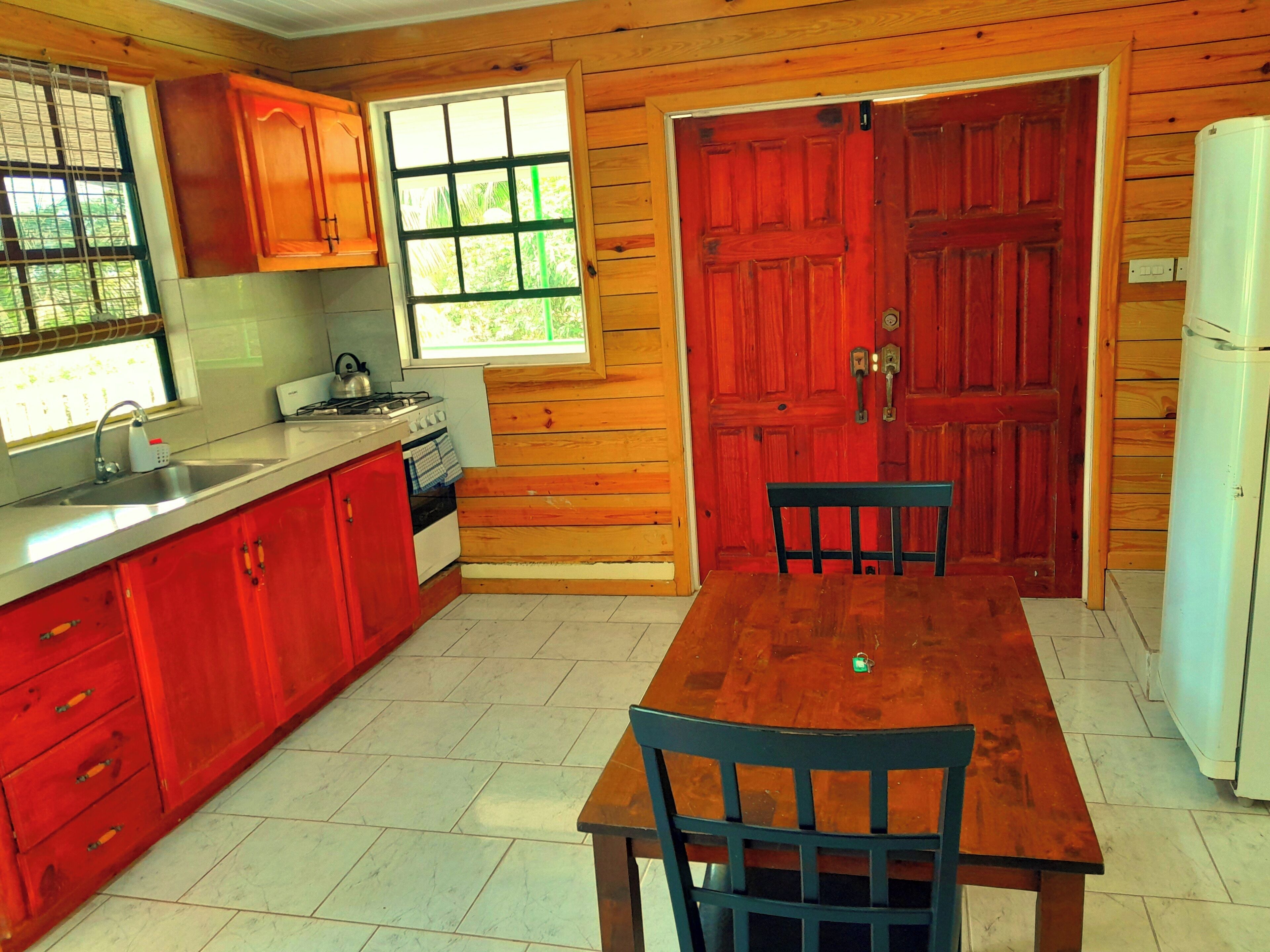 A kitchen with wooden walls, a red door, a white refrigerator, and a dining table with chairs.
