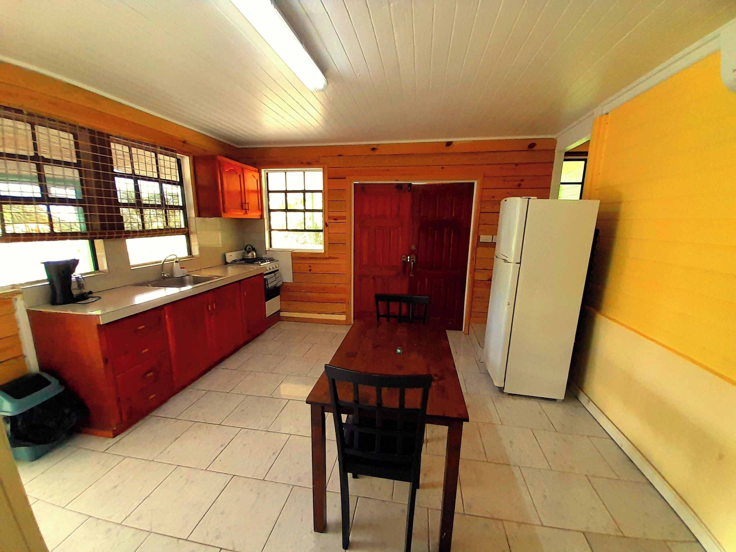 A compact kitchen with wooden cabinets, a dining table, and a refrigerator.