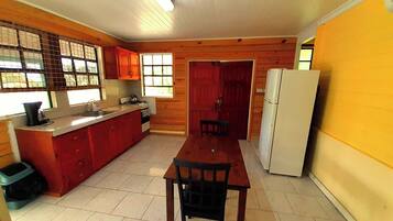 A compact kitchen with wooden cabinets, a dining table, and a refrigerator.