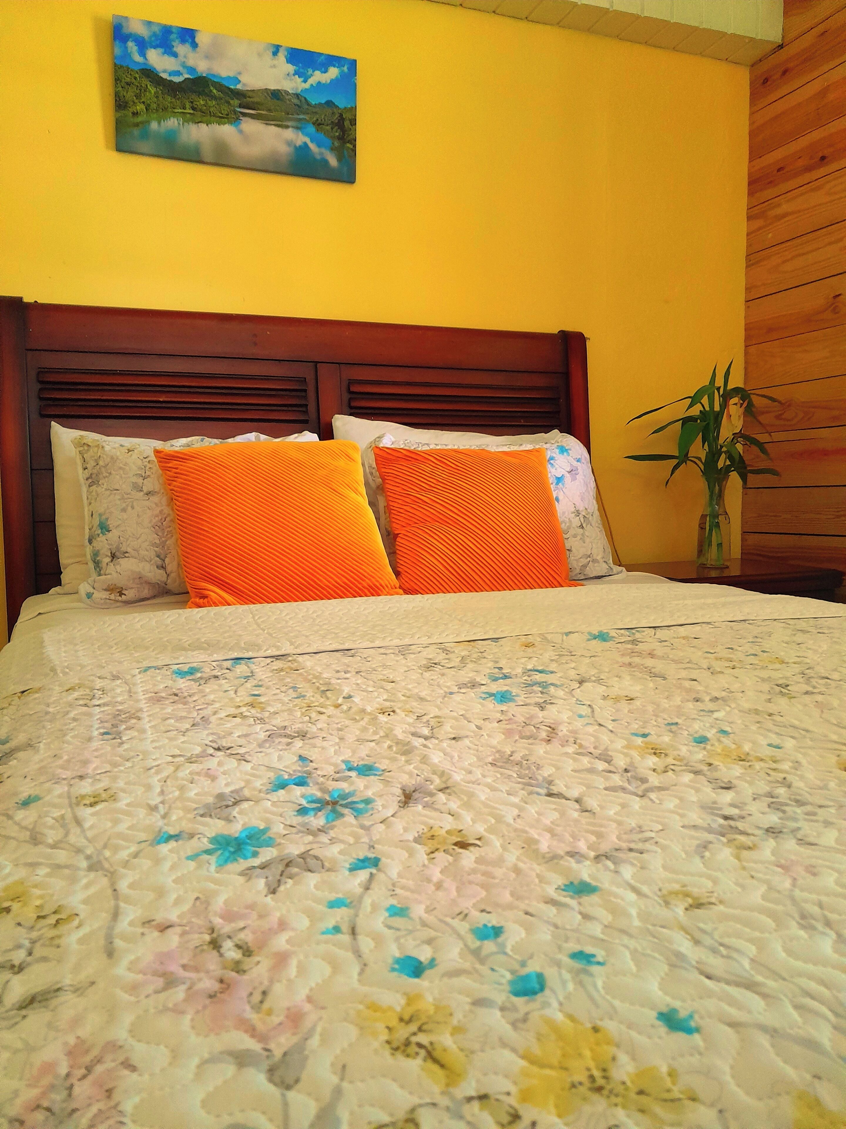 A bed with a floral quilt, two orange pillows, and a wooden headboard.