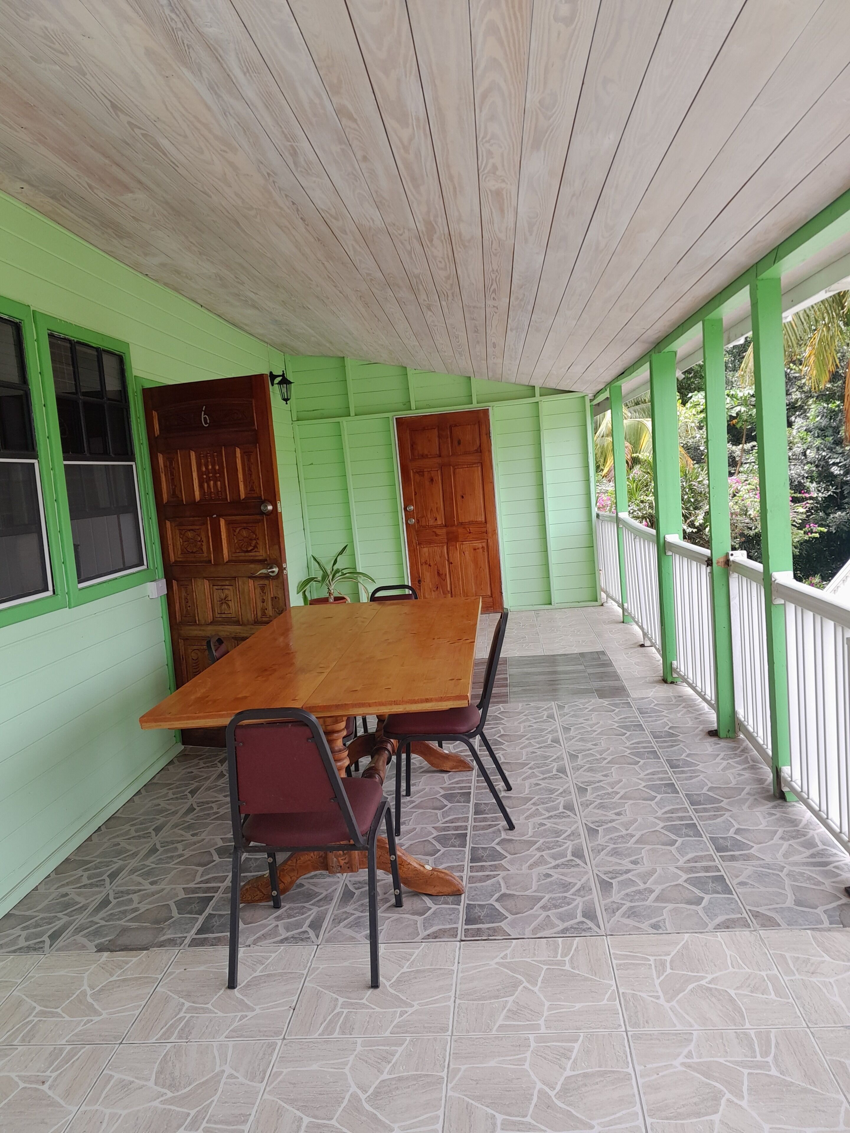 Une terrasse couverte avec une table et des chaises en bois, des murs verts et un sol carrelé.