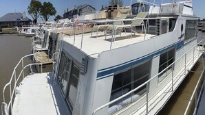 A stationary boat with a covered deck, metal railings, and a chain securing it to the dock.
