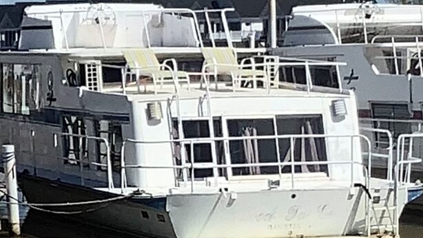 Un vaixell blanc amarrat en un port esportiu, amb diverses cobertes i baranes.