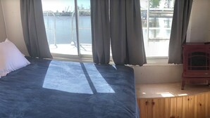 A room with a large bed, a wooden bench, and a view of a dock and water.