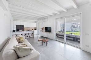 A modern living room with a sofa, a coffee table, and a TV. There is a kitchen area with cabinets and a dining table. - La Cittadella PT-6 by Wonderful Italy (Manerba del Garda)