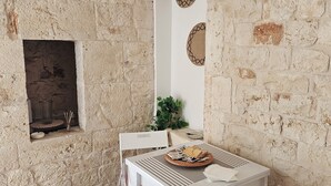 A rustic stone wall, a white table with a woven placemat, a red cushioned chair, and a small plant. - PietraRosa Apartment (Triggianello)