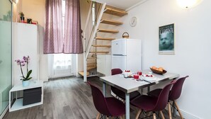 Una cucina compatta con un frigorifero bianco, un tavolo da pranzo con quattro sedie e una scala che conduce a una zona mansardata.
