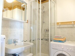 Casa de banho com cabine de duche envidraçada, lavatório e máquina de lavar roupa.