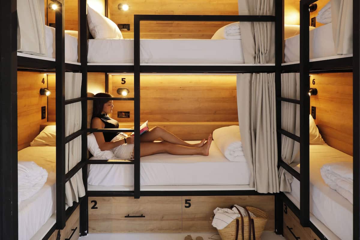 A bunk bed room with a person reading a book, wooden walls, and numbered beds.
