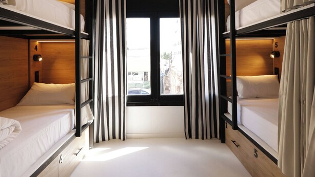 A bunk bed room with curtains, a window, and a view of the city. - BLACK AND WHITE HOSTEL (Palamós)