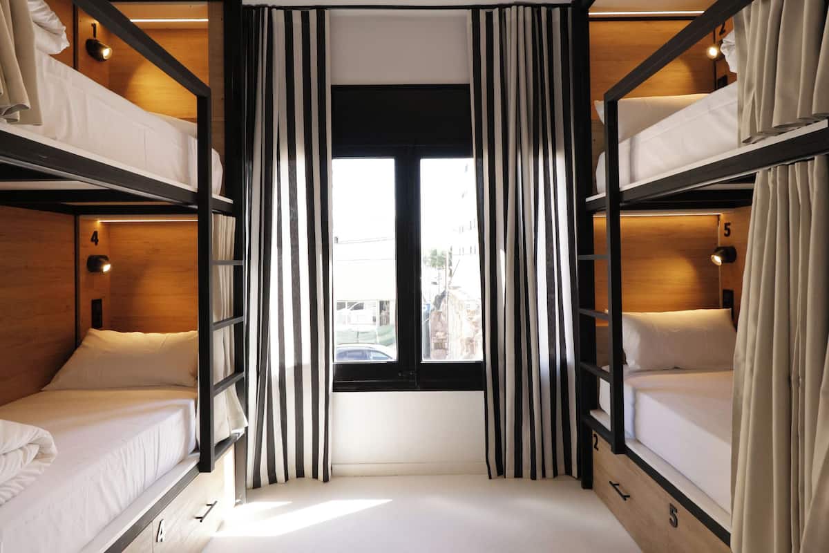 A bunk bed room with curtains, a window, and a view of the city.