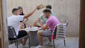 A group of people sitting around a round table in an outdoor setting with a concrete wall in the background. - BLACK AND WHITE HOSTEL (Palamós)