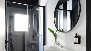 A modern bathroom with a glass shower enclosure, a white toilet, a sink, and a mirror. - BLACK AND WHITE HOSTEL (Palamós)