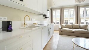 Una cucina moderna con mobili bianchi, un rubinetto dorato e una macchina per il caffè. Nell'area soggiorno, un divano beige e un tavolo rotondo in vetro.