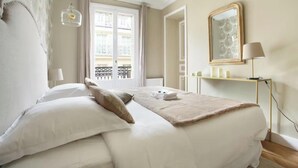 Un letto rifatto con lenzuola bianche e una coperta beige, una lampada da comodino e uno specchio a parete.