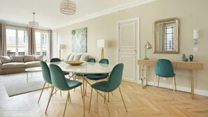 Un soggiorno spazioso con un tavolo da pranzo rotondo, sedie color petrolio, un divano beige e un'ampia finestra con vista.