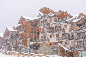 Un hôtel à plusieurs étages, doté de balcons et d’une façade en pierre, entouré de neige.