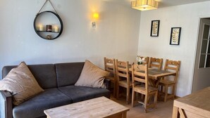 Un salon avec un canapé gris, des chaises en bois, une table basse en bois, un miroir rond et des lampes fixées au mur.
