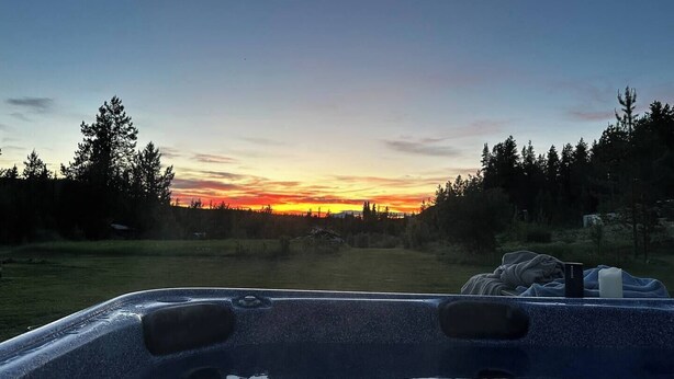 Een bubbelbad met uitzicht op een zonsondergang boven een bebost gebied.