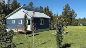 Een tweelaags huis met een blauwe gevel en een metalen dak, omgeven door een gazon en bomen.