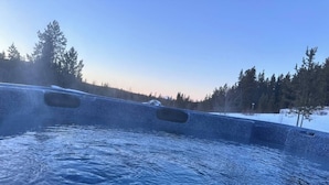 Een bubbelbad met uitzicht op een besneeuwd landschap en bomen.