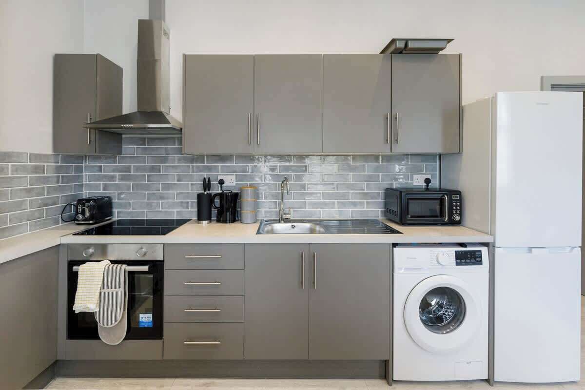 A compact kitchen with grey cabinets, a built-in microwave, a washing machine, and a sink.