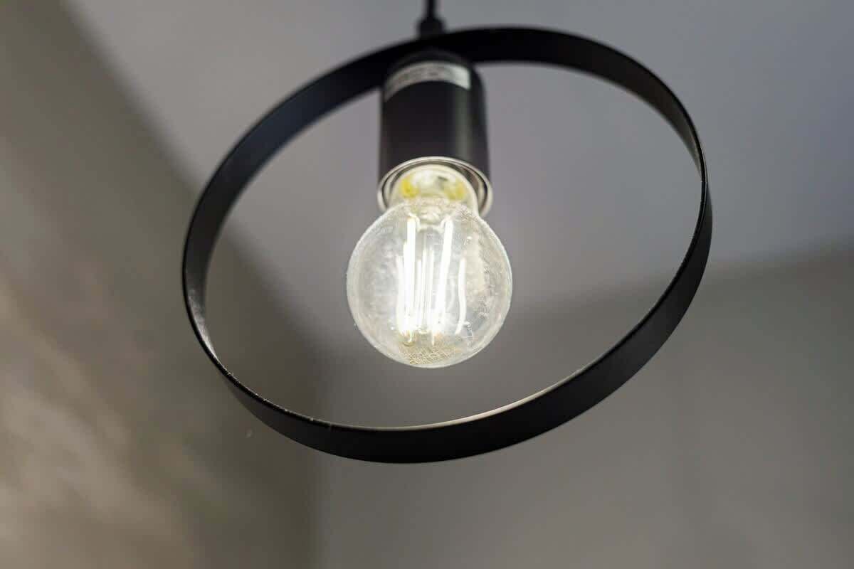 A single light bulb hanging from a black circular frame.
