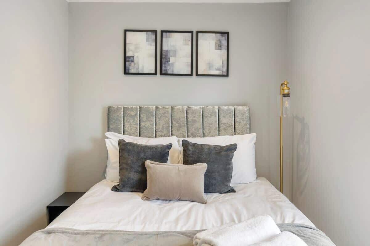 Una cama bien hecha con cabecera, una mesita de noche y tres cuadros en la pared.