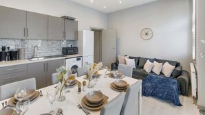 A modern kitchen with grey cabinets, a tiled backsplash, and a dining area with a table set for four. - Bright London Apartment with Central Heating (London)