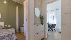 A modern bedroom with a bed, bedside tables, a dresser, and a mirror. There is a dining area with a table and chairs visible through an open doorway. - Lake River Apartment (Lecco)