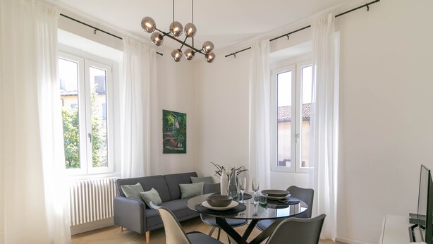 A modern living room with a gray sofa, a dining table with chairs, and a unique chandelier. - Lake River Apartment (Lecco)