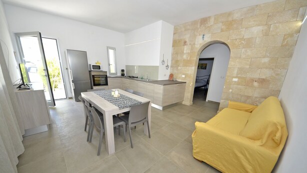 A modern kitchen with a dining area, a yellow sofa, and a stone wall. - Villa Lara (Torre Pali)